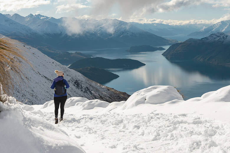 Frau wandert durch den Schnee in Neuseeland und schaut auf die Berge 