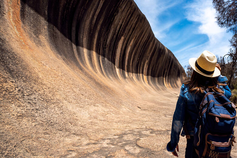 Frau mit Rucksack vor dem Wave Rock in Australien